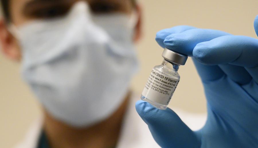 Мужчина в маске держит флакон с вакциной